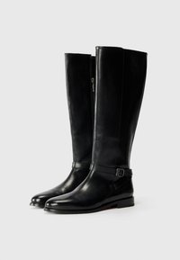 Cizme negre din piele până la genunchi, cu o textură netedă, având un fermoar pe lateral și o curea în jurul gleznei. Design cu talpă plată.