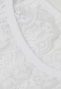 Vit spets-bh med blommönster, mjuk textur och ett slätt vitt elastiskt band längs halsringningen.