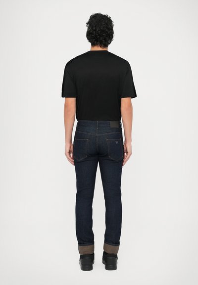 Fekete rövid ujjú póló, sötét farmernadrággal, amely kifordított szegéllyel rendelkezik. Az outfittet fekete cipő egészíti ki.