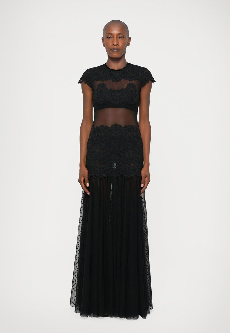 Črna prozorna čipkast vrh z kratkimi rokavi in usklajen dolg črn til krilo. Ima zapletene čipkaste vzorce in zasanjan silhuet.