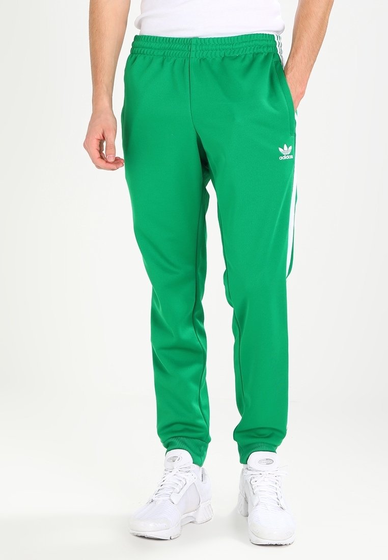 Zelené sportovní kalhoty z hladké látky s bílými pruhy po stranách a logem Adidas na levém stehně. Součástí je elastický pas.