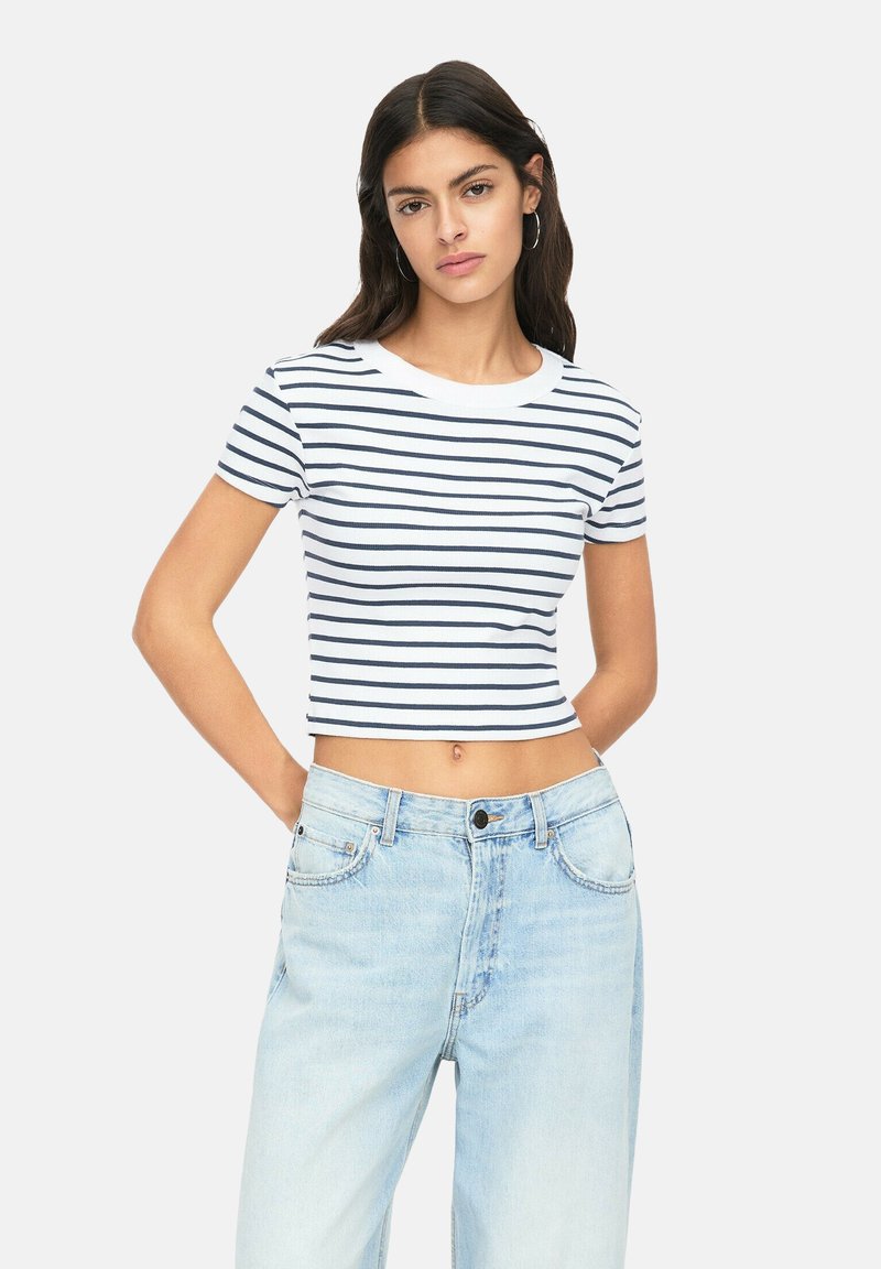 Bílý croptop s námořnickými horizontálními pruhy, kulatým výstřihem a krátkými rukávy, kombinovaný se světle modrými vysokými džíny.