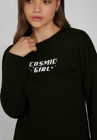 Černá mikina s dlouhými rukávy, se stiskem "COSMIC GIRL" v bílé barvě a barevnými hvězdami, měkká textura, uvolněný střih.