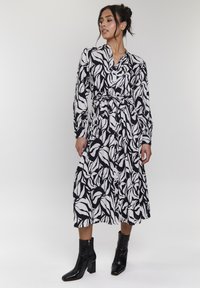 Vestito a maniche lunghe bianco e nero con un motivo floreale, cinte in vita, con scollatura a V e una gonna fluttuante al ginocchio.
