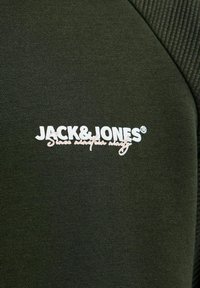 Sweatshirt vert foncé avec une texture côtelée d'un côté. Logo "JACK & JONES" en blanc affiché de manière proéminente, avec un accent en cursive en dessous.