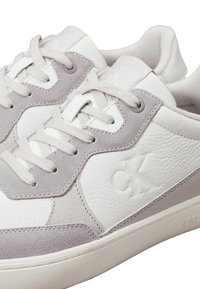Sneakers in pelle bianca e grigia con dettagli in camoscio, punta rotonda, lacci piatti e logo impresso sul lato e sulla linguetta.