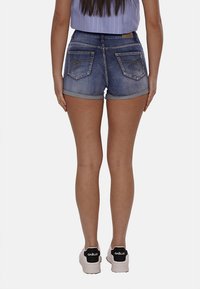 Bermuda di jeans in un lavaggio blu rovinato con orli arrotolati, dotate di due tasche posteriori con cuciture decorative. Abbinate a sneakers bianche.
