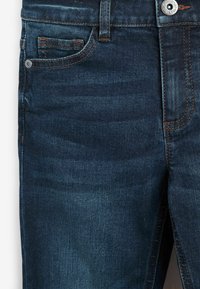 Donkerblauwe denim jeans met oranjerode stiksels, voorzien van een voorzak, metalen knoopsluiting en een gladde textuur. Eenvoudig ontwerp, rechtvallende pasvorm.