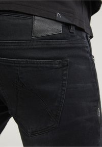 Svarta denimjeans med en subtil glans, med en distinkt patch märkt 'CHASIN' och en unik fickdesign. Slät textur och skräddarsydd passform.