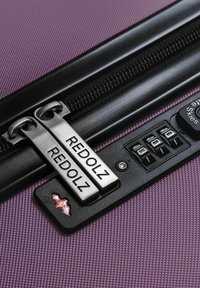 Primo piano della cerniera di una valigia viola bloccata con un lucchetto che mostra il nome del marchio "REDOLZ" e un lucchetto a combinazione a tre cifre impostato su 000.