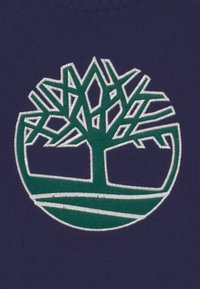 Granatowa dzianina ma wyróżniające się zielone i białe haftowane logo drzewa z misternie wykonanymi gałęziami oraz okrągłą podstawą.