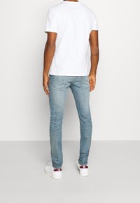 Vit kortärmad t-shirt för män i kombination med ljusblå jeans, med en slim fit och subtila slitningar. Bärs med vita sneakers.