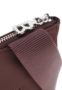 Borsa in tessuto color mogano con una tracolla texture, dotata di una cerniera e un tirante in argento. Il design è compatto e pratico per l'uso quotidiano.