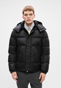 Μαύρο puffer μπουφάν με υφή, διαθέτει φερμουάρ μπροστά, κουκούλα και δύο μπροστινές τσέπες. Σχεδιασμένο με κανονική εφαρμογή και ελαστικούς καρπούς.