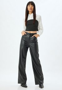 Zwarte leren broek met wijde pijpen, gecombineerd met een korte zwarte pinstripe-top, gedragen over een witte blouse met knoopsluiting. Rechte silhouet, minimalistische details.