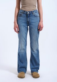 Vaaleat denim-farkut, joissa on leveät lahkeet, viisi taskua ja kevyesti haalistunut pinta. Yhdistettynä ruskeisiin mokkanahkasaappaisiin.