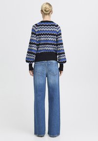 Stickad tröja med blå och svart zigzag-mönster, ballongsärmar och ribbade mudd. Matchad med högmidjade ljusblå vida jeans.