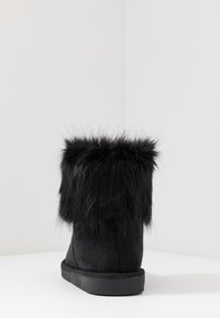 Czarne zamszowe botki za kostkę z futrzanym mankietem. Okrągły nosek, płaska podeszwa i miękka faktura. Mankiet ma długie, puszyste włókna jako dodatkowy detal.