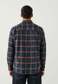Chemise en flanelle à carreaux bleu foncé avec des accents rouges et beiges. Elle dispose de manches longues, d'un col et d'une coupe droite.
