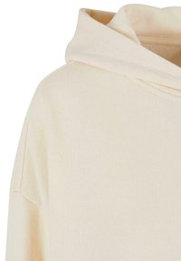 Krémová mikina s kapucí vyrobená z měkké látky. Má volný střih, viditelné stehy a útulnou, př oversized kapuci.