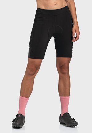 Schwarze Fahrradhosen mit gepolsterter Einlage, ausgestattet mit einer glatten Textur und passgenauem Design. Kombiniert mit pinken Socken und schwarzen Fahrradierschuhen.
