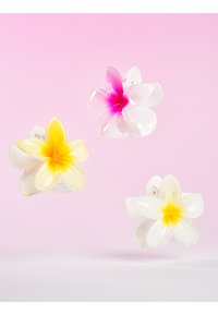 Tre hårklämmor formade som blommor: en vit med rosa centrum, en vit med gult centrum och en vit med gul gradient. Genomskinlig plast.