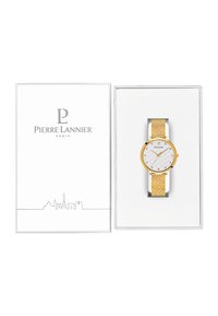 Reloj dorado con correa amarilla texturizada y esfera blanca acolchada. Presentado en una caja blanca con el logotipo "Pierre Lannier" y el horizonte de París.