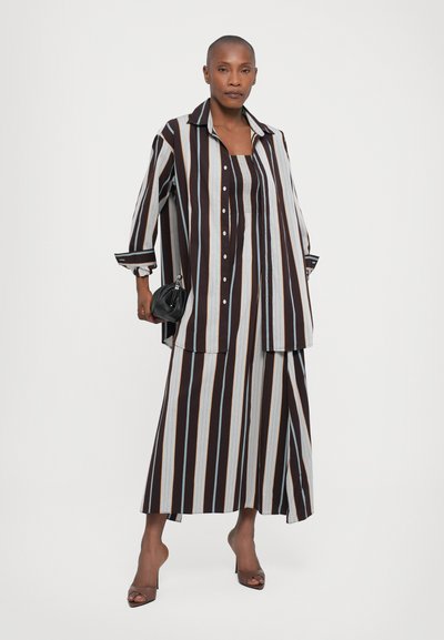 Striped brown, blue, and cream shirt dress with a collar, button closure, and long sleeves, paired with a matching skirt and black handbag.