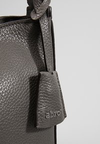 Gros plan d'un sac à main en cuir gris texturé avec une étiquette attachée embossée du nom de la marque "abro".