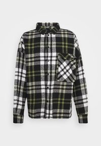 Camicia in flanella a quadri nera, bianca e verde con chiusura a bottoni, colletto, maniche lunghe e taschino frontale che presenta un motivo a quadri diagonali.
