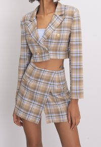 Blazer droit à carreaux marron et bleu avec des boutons dorés et des manches longues, assorti d'une mini jupe à carreaux avec poches latérales.