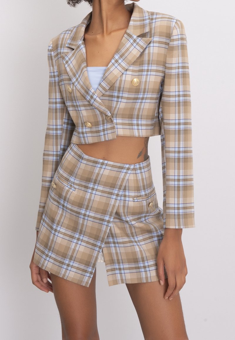 Blazer droit à carreaux marron et bleu avec des boutons dorés et des manches longues, assorti d'une mini jupe à carreaux avec poches latérales.