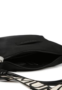 Czarna torba na zamek błyskawiczny o gładkiej fakturze, z plecionym uchwytem w geometryczny wzór i materiałową metką z przodu.