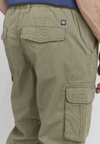 Pantalons cargo vert olive en tissu texturé, dotés de deux poches arrière et de poches cargo sur les côtés. Avec une étiquette logo près de la taille.