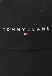 Sort kasket lavet af glat stof med "TOMMYJEANS" broderet i hvidt og et lille rødt, hvidt og blåt flaglogo.