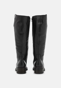 Ein Paar schwarze Lederkniehohe Stiefel mit niedrigen Blockabsätzen, von hinten auf einem schlichten hellen Hintergrund betrachtet.