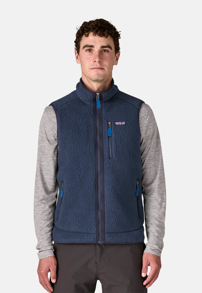 Gilet in pile di colore blu scuro con collo alto, frontale con zip e tasche laterali. Presenta maniche lunghe grigie e dettagli a zip blu.