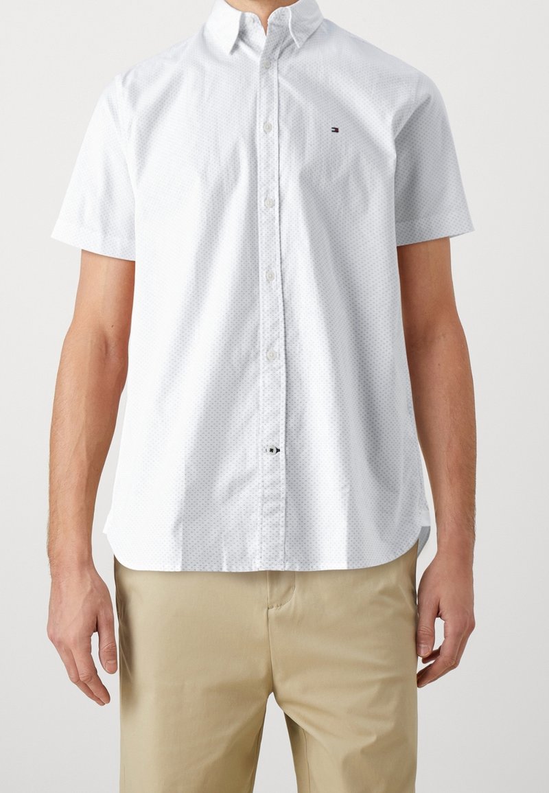 Hvid kortærmet button-up skjorte med et subtilt prikkemønster, krave og logo-accent, parret med lysekhaki bukser.