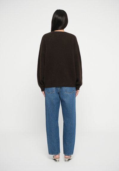 Brun oversized sweater med rund hals, parret med højtaljede blå denim jeans, med lige ben og baglommer.