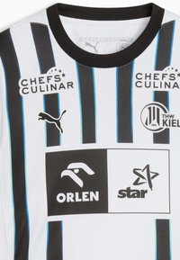 Bela športna dresa z črnimi in modrimi navpičnimi črtami. Vsebuje logotipe: Puma, Chefs Culinar, Orlen in zvezda. Okrogla črna ovratnica.