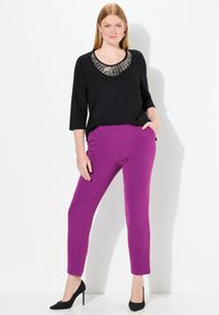 Top nero con scollatura di perline, maniche a tre quarti; pantaloni aderenti viola con tasche laterali; indossati con tacchi a punta neri.