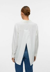 Hvid langærmet skjorte med split bagdesign, krave, knapærmer og en glat tekstur, parret med blå denim jeans.