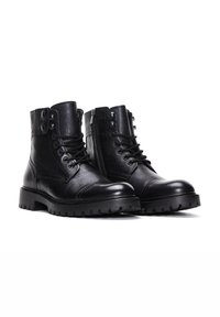 Botas de cuero negras hasta el tobillo con acabado texturizado, cordones en la parte frontal y cremallera lateral. Presentan suelas robustas y tachuelas decorativas en el cuello.
