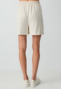 Lichtbeige shorts met een elastische tailleband, met een ontspannen pasvorm en een simpele zoom. Gemaakt met witte sneakers.