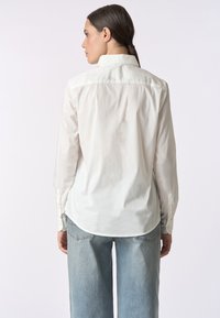 Camicia bianca a maniche lunghe con colletto classico, orlo curvo, polsini abbottonati e vestibilità sartoriale. Realizzata in tessuto di cotone.