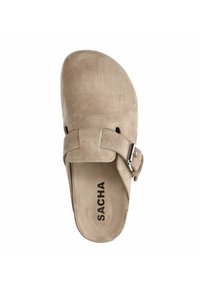 Beige suède klompen met een ronde neus, verstelbare band en een metalen gesp accent. Beschikt over een opvallende "SACHA" branding aan de binnenkant van de inlegzool.