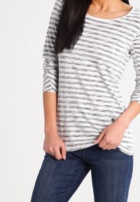 Gestreiftes Langarmshirt aus weichem Stoff, mit schwarzen und grauen horizontalen Streifen auf weißem Hintergrund. Rundhalsausschnitt, lockere Passform.