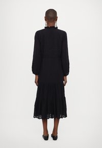 Vestido maxi preto com mangas longas, decote em babados, corpete bordado e saia em camadas. Textura suave com detalhes em tule na barra.