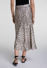 Falda midi de satén con estampado de leopardo y dobladillo acampanado. Presenta una textura suave y una cintura ajustada. Se lleva con sandalias negras de tiras.