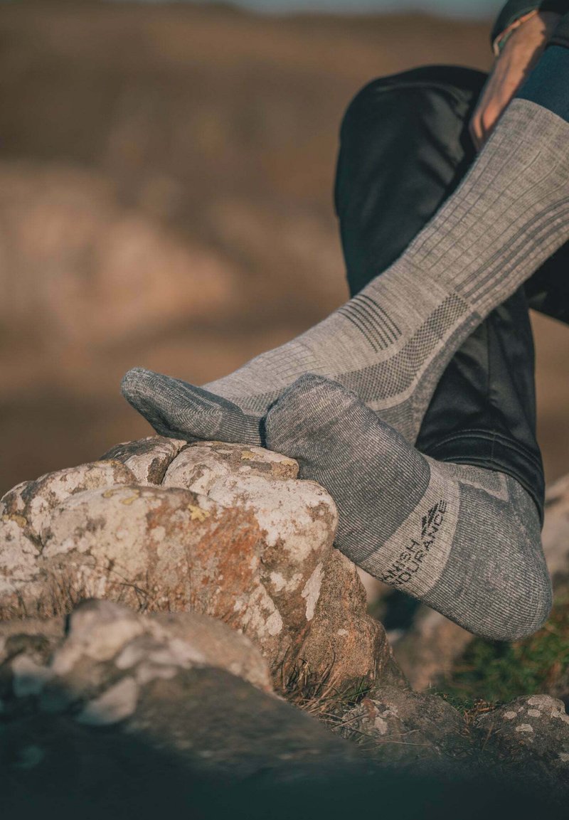 Calcetines de lana gris con un patrón de punto texturizado, que presentan la puntera y el talón reforzados, usados sobre una superficie rocosa.